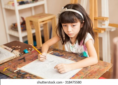 Portrait d'une jolie petite brune pensant et essayant de s'inspirer pour dessiner dans une classe d'art : photo de stock