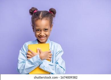 Portrait Of Pretty Little Child With Book Isolated Over Purple Background. Happy Girl With Curly Hair Go In 1st Grade At School.Back To School, Elementary School