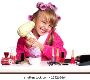 Portrait of pretty little girl seating at table with makeup accessories on white background