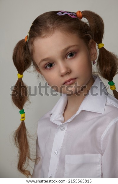 portrait of a pretty little girl in a white\
shirt and pigtails with colored rubber\
bands