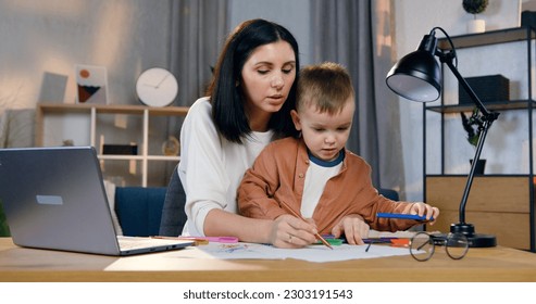 Portrait pretty loving caring 30  aged woman which holding small attantive son knees   helping him to draw beautiful picture