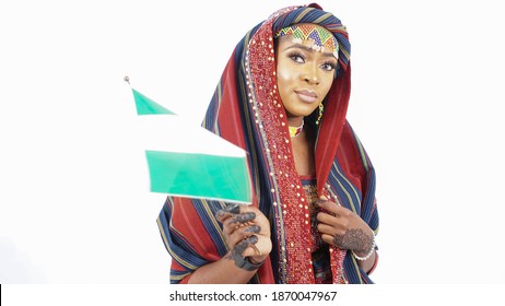 Portrait of pretty Nigerian Hausa woman dressed in traditional attire and waving the national flag