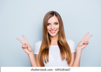 Portrait of pretty positive girl with beaming smile gesturing two v-signs, peace symbols isolated on grey background looking at camera