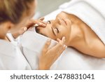 Portrait of pretty relaxed young woman lying with closed eyes having facial massage in spa salon. Female client enjoy receiving skin care procedure treatment. Wellness and beauty day concept.