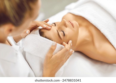 Portrait of pretty relaxed young woman lying with closed eyes having facial massage in spa salon. Female client enjoy receiving skin care procedure treatment. Wellness and beauty day concept.