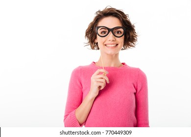 Portrait of a pretty smiling girl holding paper eyeglasses at her face isolated over white background