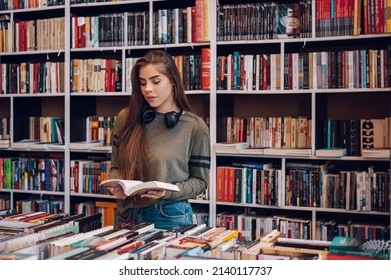 Portrait of a pretty smiling girl reading book while buying in a bookstore. Choosing a good book to buy in a bookstore. Woman interested in a book.