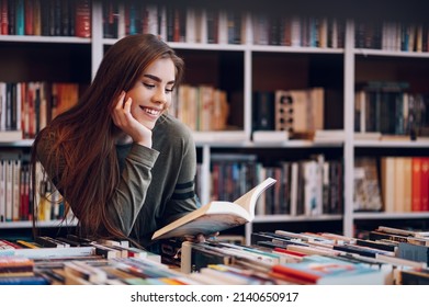 Portrait of a pretty smiling girl reading book while buying in a bookstore. Choosing a good book to buy in a bookstore. Woman interested in a book.