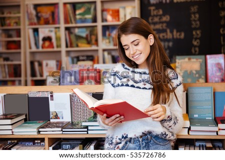 Portrait of a pretty smiling girl reading book indoors in library