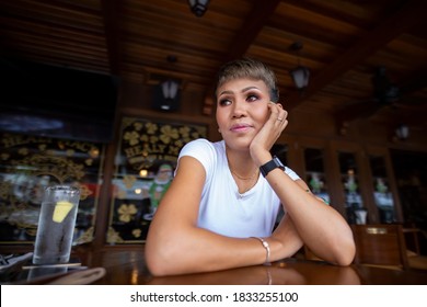 Porträt einer ziemlich lächelnden malaysischen Frau, sitzend an einem Tisch in einem Café in Kuala Lumpur, Malaysia. Ein junges charmantes asiatisches Mädchen, das allein an einem Holztisch in einem Restaurant sitzt.  