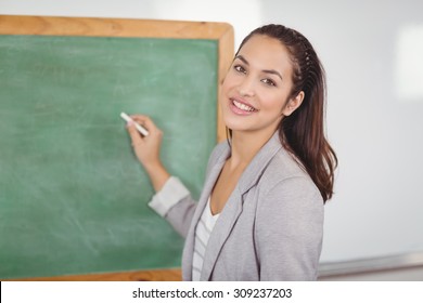 Portrait Of Pretty Teacher Writing On Chalkboard In A Classroom In School