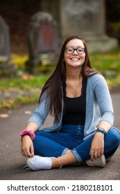 Portrait Of A Pretty Teenaged Girl With Dark Hair And Glasses Seated In A Cemetery