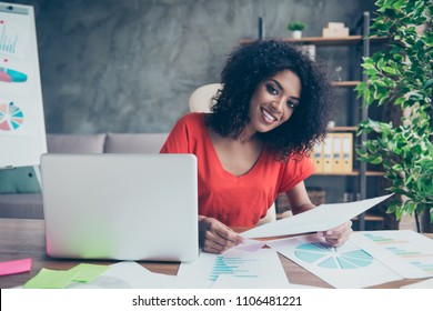 Portrait of pretty trendy woman with beaming smile in vivid outfit sitting at desk in modern office holding document in hand looking at camera. Study education university knowledge concept