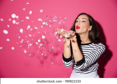 Portrait of a pretty woman blowing confetti from her hands isolated over pink background - Powered by Shutterstock