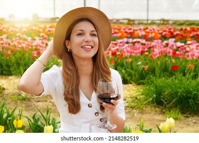 Portrait of pretty woman drinking glass of red wine over flowered background looking to the side with happy face smiling