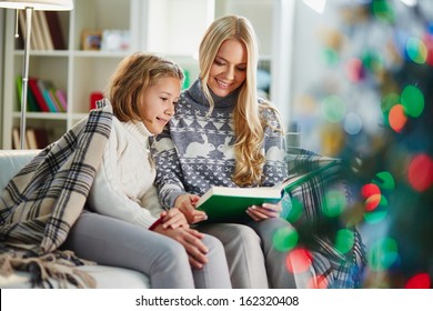 Portrait of pretty woman and her daughter reading book on Christmas evening - Shutterstock ID 162320408