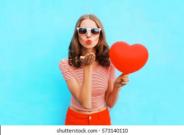 Portrait pretty woman sends air kiss with red balloon heart shape over blue background