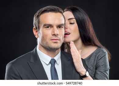 Portrait Of Pretty Woman Whispering In Ear Of Handsome Man Isolated On Black