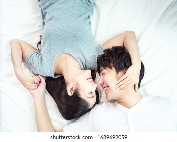 Portrait of pretty young asian couple with happiness. asia man and woman lay on bed facing together with big smile hand cover face each other.