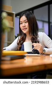 Portrait, Pretty Young Asian Female Sipping Her Morning Coffee During Woking In Her Office Room.