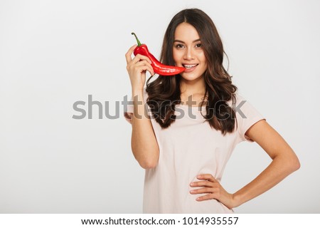 Portrait of a pretty young asian woman biting chili pepper isolated over white background