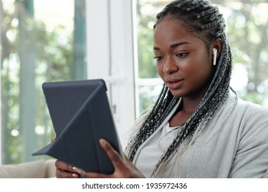 Portrait Of Pretty Young Black Woman With Braided Hair Wearing Earbuds And Videocalling Her Friend Of Family Member