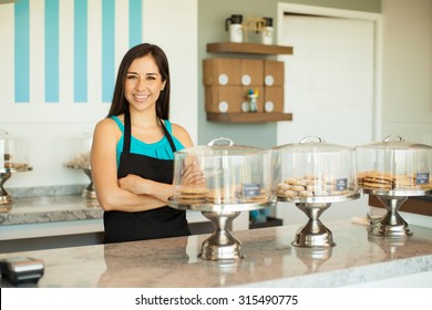 Portrait of a pretty young brunette in an apron selling cookies and pastries in a cake shop