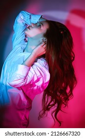 Portrait Of A Pretty Young Girl With Long Hair In White Shirt Looking Up With Hope Illuminated By A Beam Of Light. Thoughtfulness, Insight. Studio Portrait In Crimson Lighting.