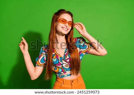Portrait of pretty young girl touch sunglass dance wear top isolated on bright green color background