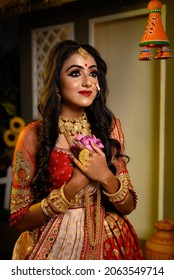 Portrait Of Pretty Young Indian Girl Wearing Traditional Saree, Gold Jewellery And Bangles Holding Lotus Flower In Her Hands In Studio Lighting Indoor. Indian Culture, Occasion, Religion And Fashion.