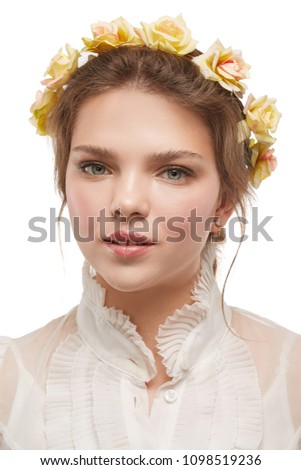 Portrait of a pretty young lady with a boho flower crown, in a white retro blouse. The girl looking pensively at the camera on the white background, her mouth slightly open, yellow roses in her hair.