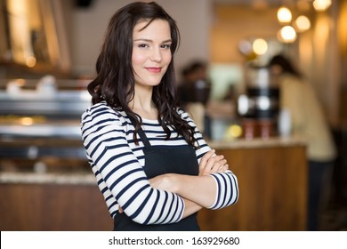 Portrait Of Pretty Young Waitress Standing Arms Crossed In Cafeteria