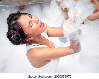Portrait of pretty young woman in bikini having fun on soap foam disco party in the swimming pool.