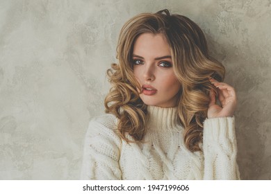 Portrait of pretty young woman with blonde curly hair on gray background