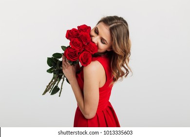 Portrait of a pretty young woman dressed in red dress holding bouquet of roses isolated over white background