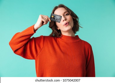 Portrait of a pretty young woman dressed in sweater holding credit card at her face isolated over blue background - Shutterstock ID 1075042007
