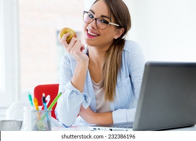 Portrait Of Pretty Young Woman Eating An Apple In Her Office.