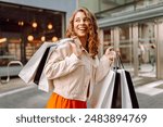 Portrait of pretty young woman walking down with shopping bags on city street. Consumerism, sale, purchases, shopping, lifestyle concept.