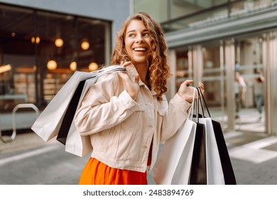 Portrait of pretty young woman walking down with shopping bags on city street. Consumerism, sale, purchases, shopping, lifestyle concept. - Powered by Shutterstock