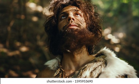 Portrait of Primeval Caveman Wearing Animal Skin Raises Hands to Heaven Looking at the Sun, Having Pagan Religious Experience. Prehistoric Neanderthal Believing and Praying to God. High Angle Shot