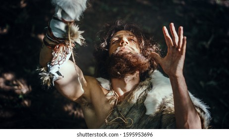 Portrait of Primeval Caveman Wearing Animal Skin Raises Hands to Heaven Looking at the Sun, Having Pagan Religious Experience. Prehistoric Neanderthal Believing and Praying to God. High Angle Shot