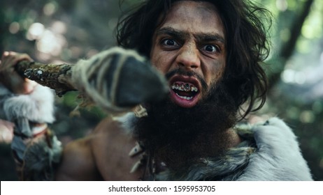 Portrait of Primeval Caveman Wearing Animal Skin and Fur Hunting with a Stone Tipped Spear in the Prehistoric Forest. Prehistoric Neanderthal Screaming, Threatening and Attacking