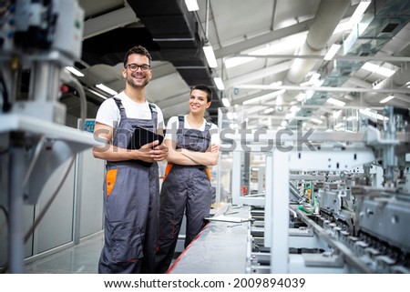 Portrait of production line workers controlling manufacturing process of modern packaging industrial machine in printing factory.