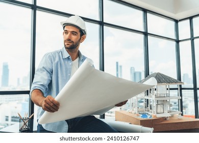 Portrait of professional architect engineer looking at camera while reading project plan at house model and architect equipment with skyscraper. Interior surrounded by architect studio. Tracery. - Powered by Shutterstock