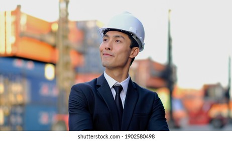 Portrait of Professional asian businessman, Industry Engineer, Worker Wearing suit with white Hard Hat standing with confidence in the background of unfocused industrial containers yard workplaces .