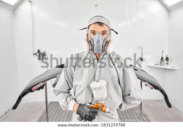 Portrait of professional auto painter.\
Worker painting parts of the car in special painting chamber,\
wearing costume and protective gear. Car service\
station.