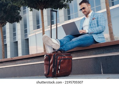 Portrait Of Professional Businessperson Typing On Laptop Sitting On Bench In City.