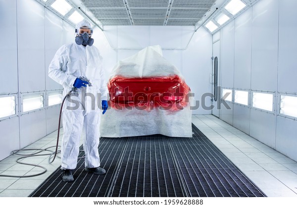 Portrait of professional car\
painter holding painting gun and standing by automobile in the\
chamber.