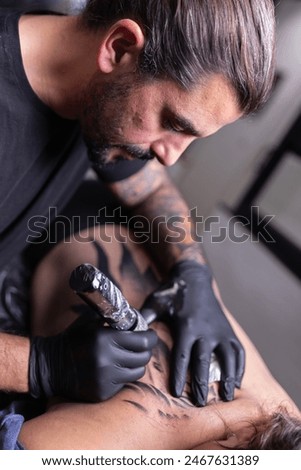 Portrait of a professional creative tattoo master in gloves doing wing tattoo on the back of a young woman in a tattoo parlor. Process of making tattoos with a machine.
