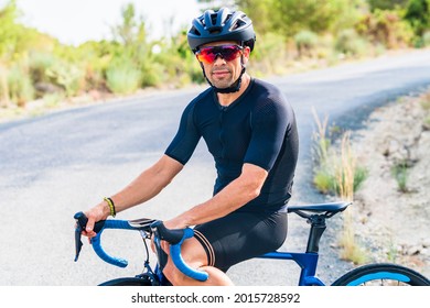 Portrait Of Professional Cyclist Resting Sitting On The Bicycle Dressed In Black Sportswear And Helmet